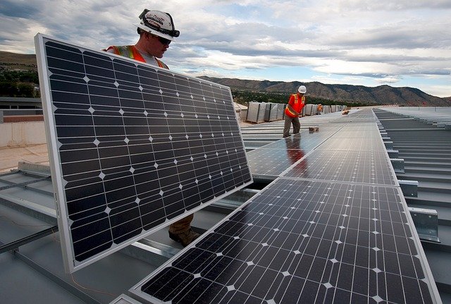 2 ouvriers en tenue de chantier en train d'installer des panneaux solaires sur une toiture