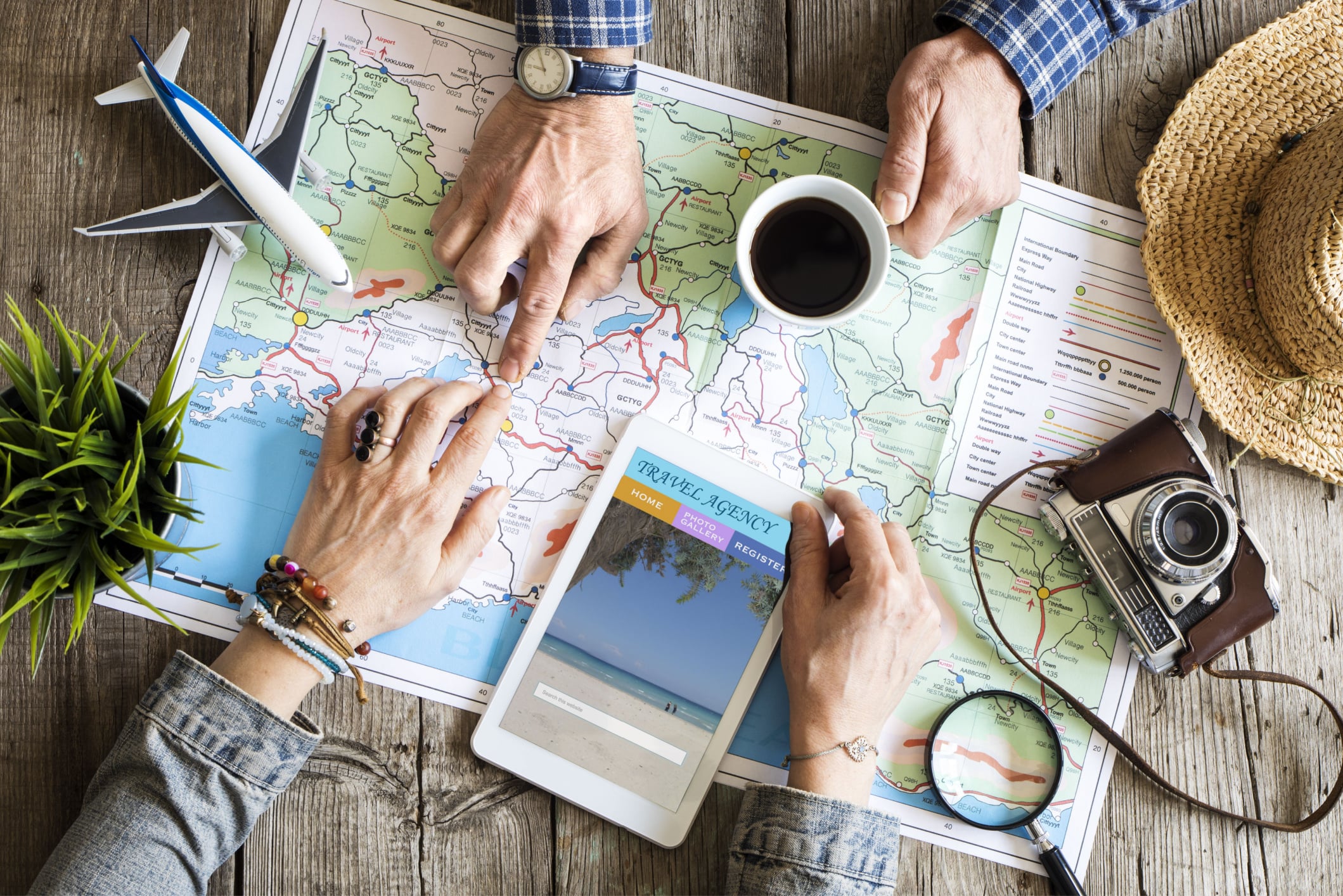 carte étalée sur une table avec les mains d'un couple en train de planifier leur prochain voyage en pointant une destination sur la carte