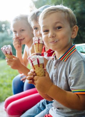 Trois enfants souriants en train de manger une glace sur un banc dans un parc
