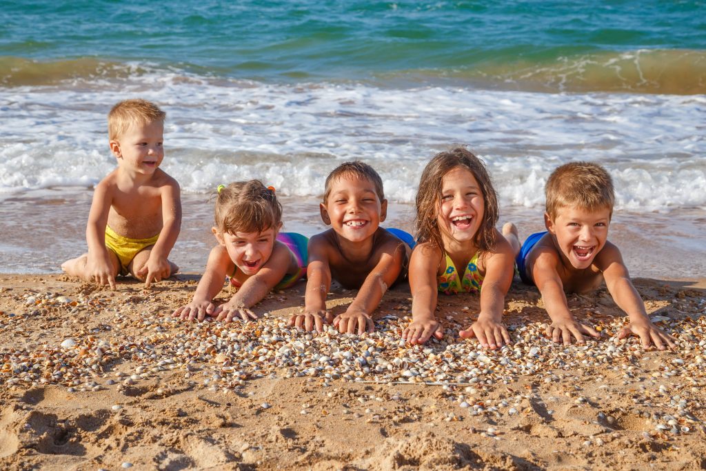 5 enfants souriants couchés sur une plage de sable blanc 
