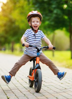 petit garçon sur un vélo avec un casque orange en train de rigoler dans un parc