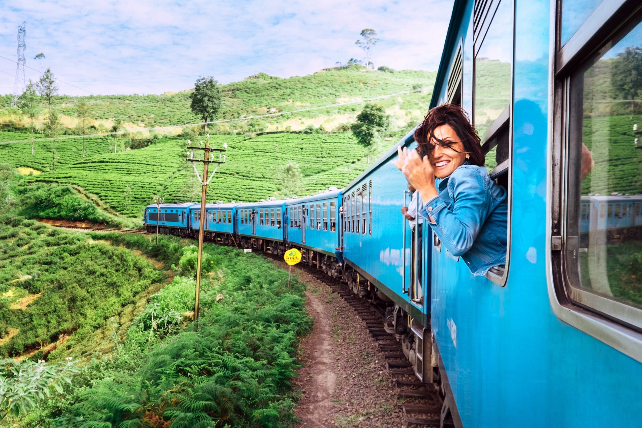 femme passant sa tête à l'extérieur dans un train bleu parcourant des paysages verdoyant