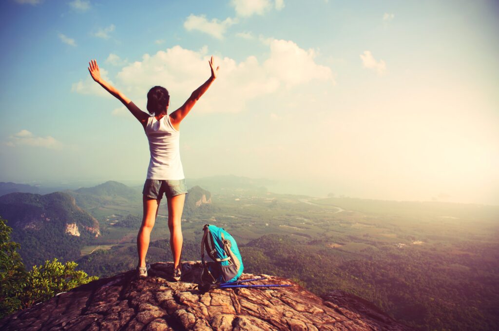 femme en train de poser les mains en l'air après une randonnée en haut d'une montagne