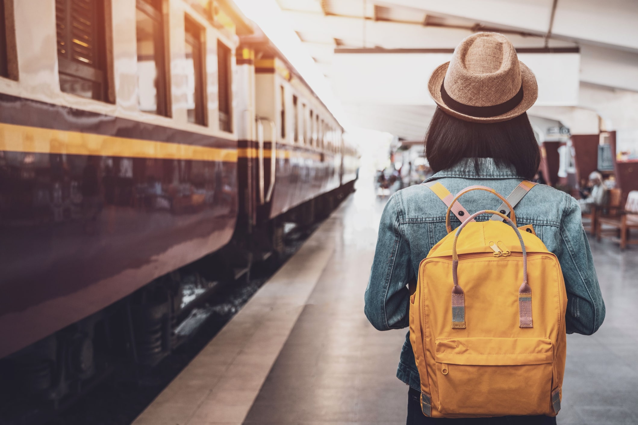 femme de dos avec un sac à dos jaune sur le quai d'une gare en train de rentrer de vacances