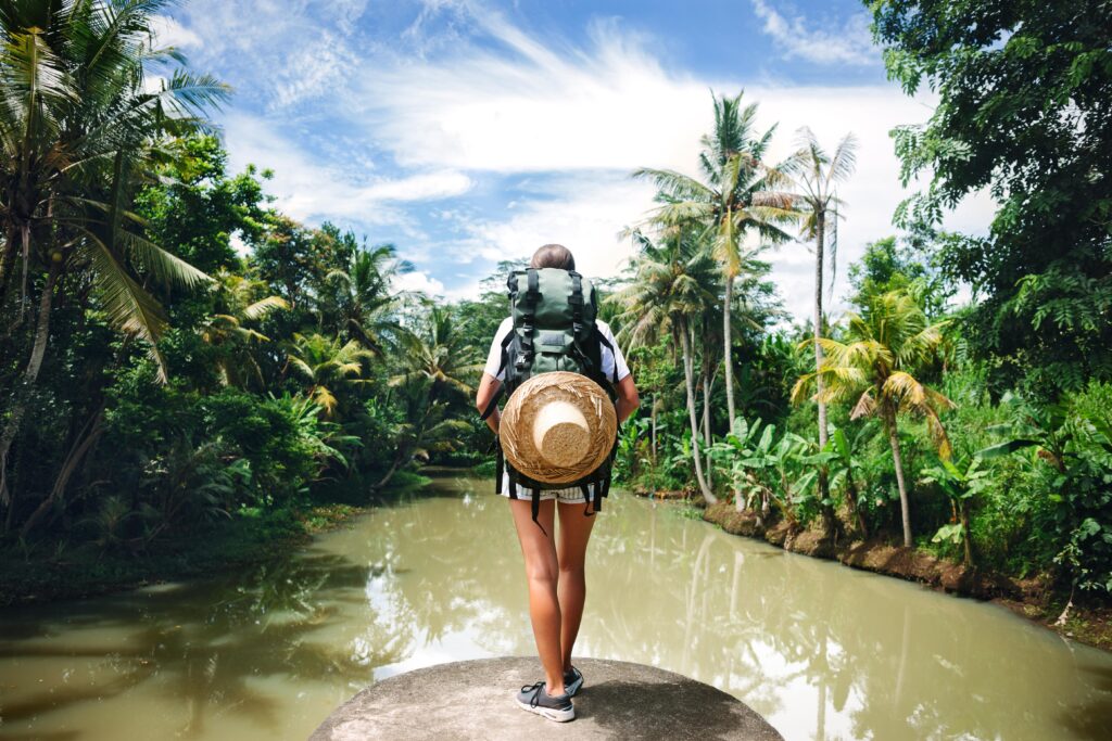 femme en sac à dos en train de contempler un fleuve et une jungle pendant son voyage itinérant