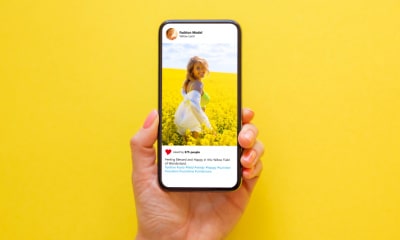 main d'une femme tenant un téléphone avec une publication instagram ouverte représentant une photo d'une fille en vacances dans un champs de fleurs jaunes.