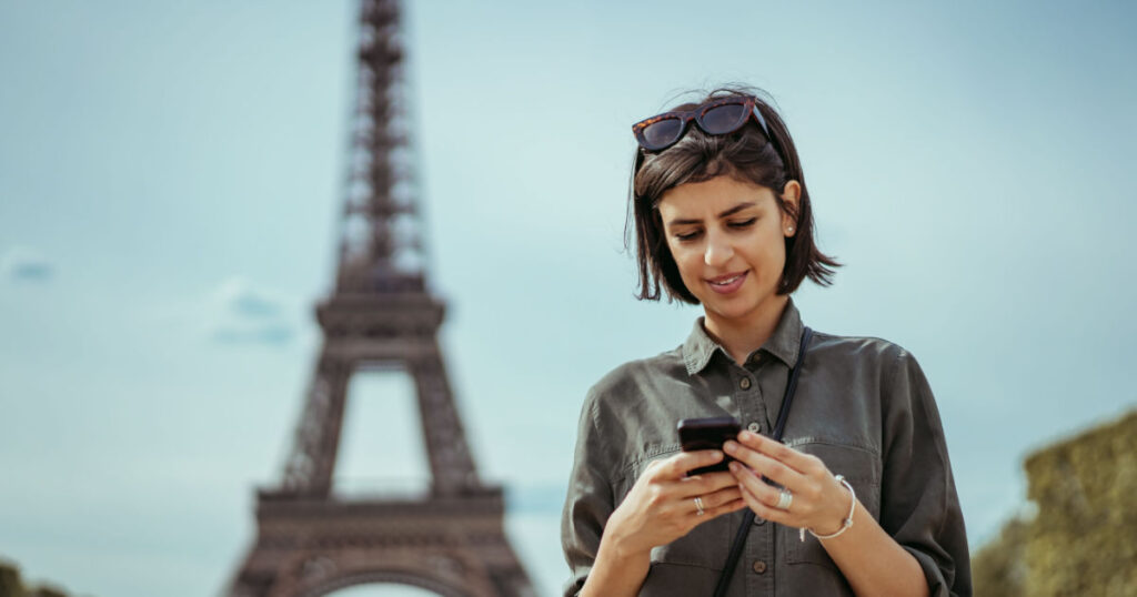 femme voyageuse en train de regarder son téléphone avec ses applications de voyage devant la tour Eiffel