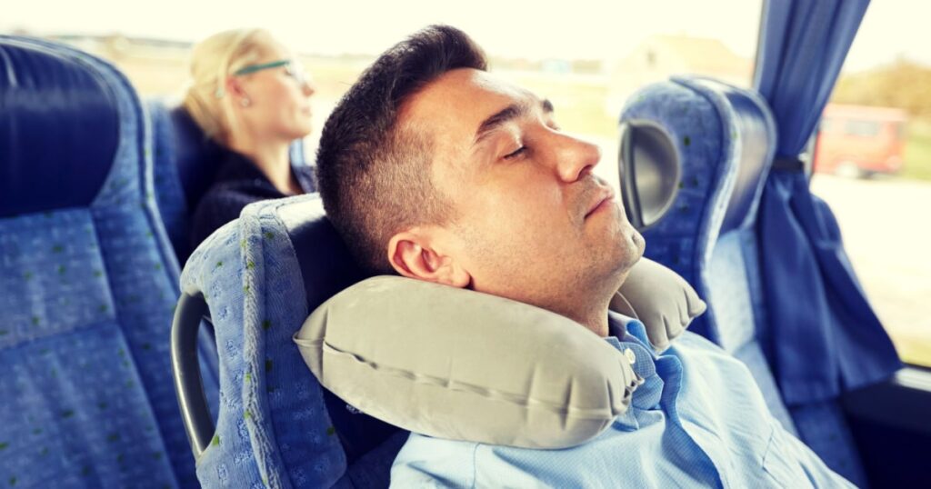 coussin de voyage gonflable gris utilise par un homme en train de dormir dans un bus