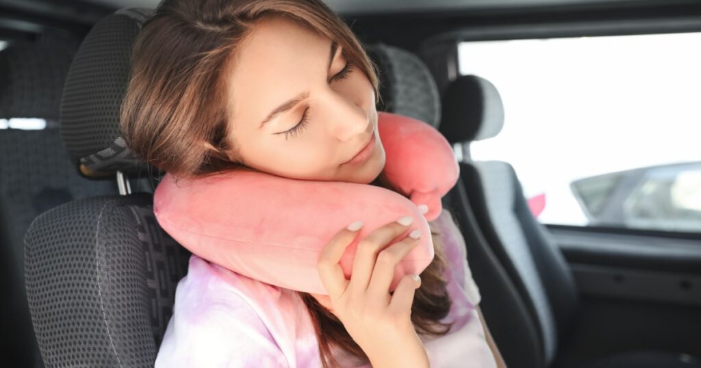coussin de voyage rose à mémoire de forme utilisée par une jeune femme en train de dormir à bord d'une voiture 8 places