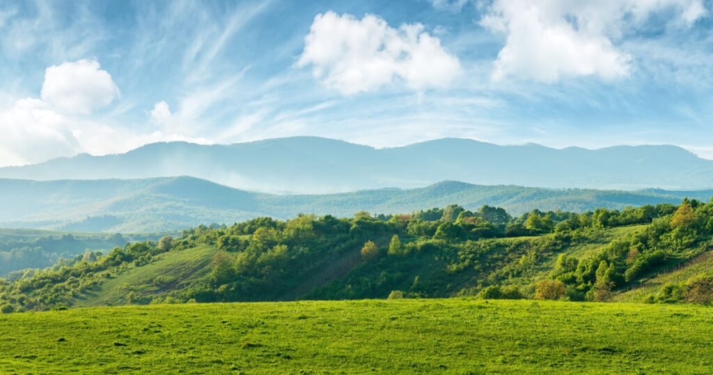 photo panorama d'un paysage montagneux montrant différents plans : de la verdure, la coline d'en face et les montagnes en fond