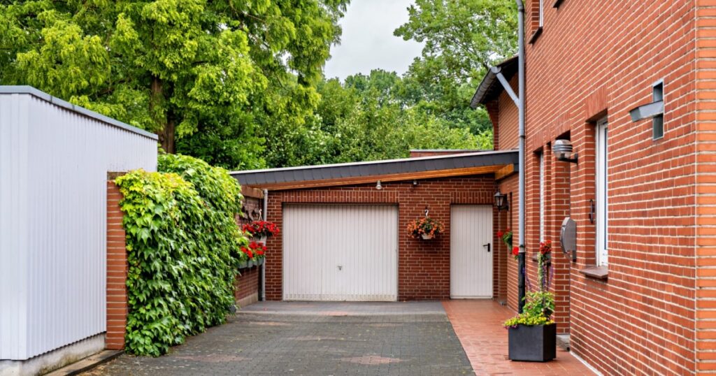 porte de garage battante en PVC blanc attenante à une maison en brique rouge