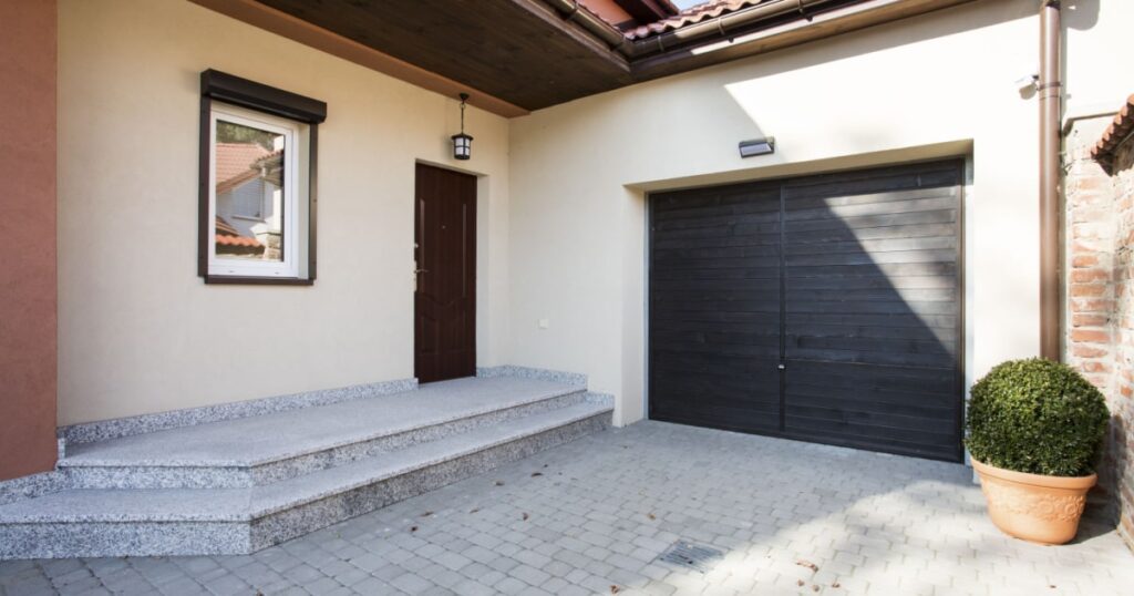 porte de garage en bois noire attenante à une maison en crepi blanc